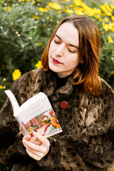 Une  femme rousse lit un livre devant un buisson de fleurs jaunes lors d'une séance photo portrait à Toulouse.