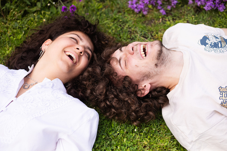 Un frère et une sœur allongés dans l'herbe et qui rigolent.