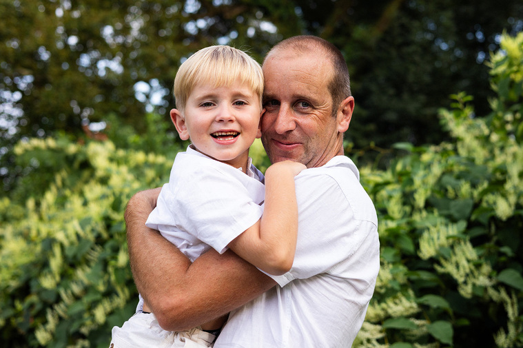 Un père tenant son fils blond et souriant dans les bras.