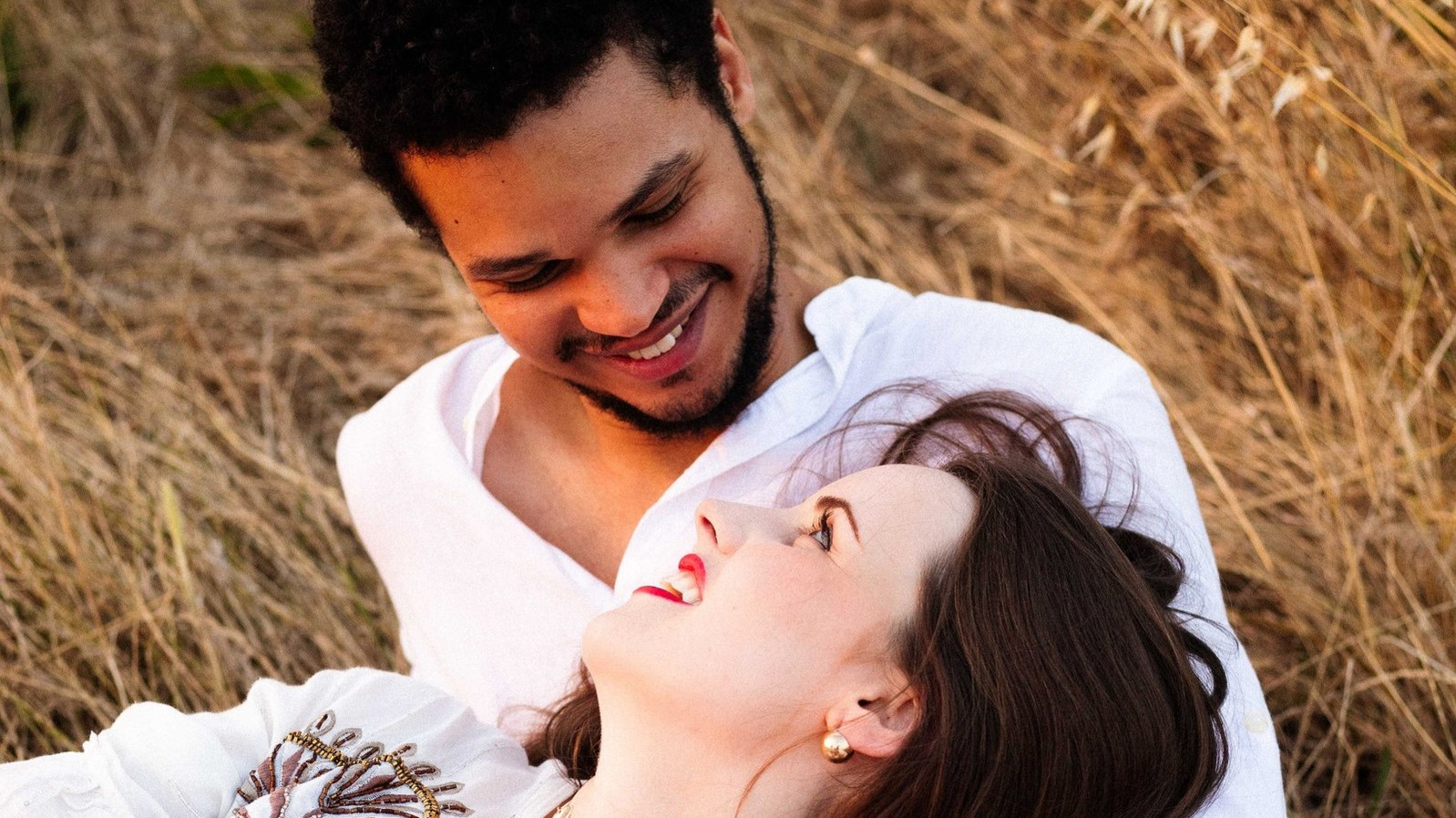 Un couple se regarde amoureusement et sont allongés sur de l'herbe sèche.
