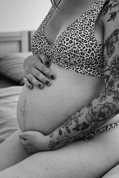 Une femme enceinte est assise sur un lit et se tient le ventre lors d'une séance photo grossesse à Toulouse