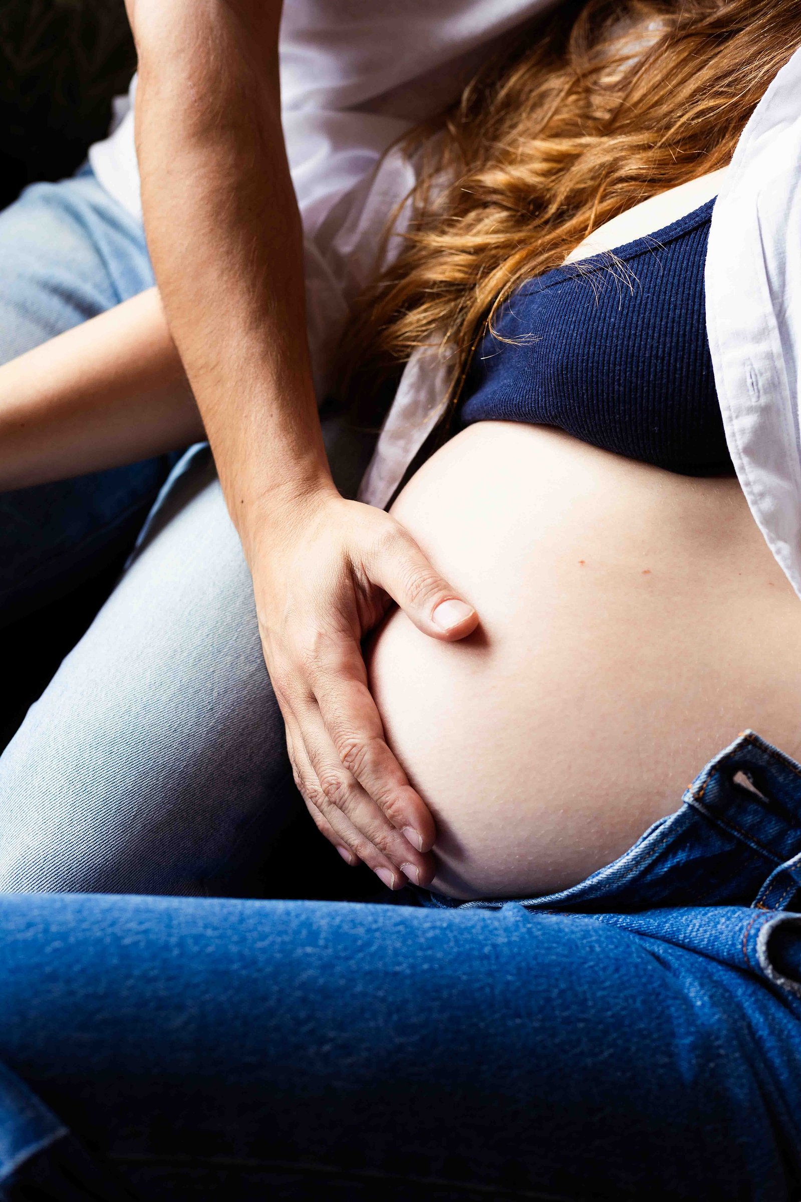 Le ventre d'une femme enceinte et la main de son mari lors d'une séance photo grossesse à Toulouse.