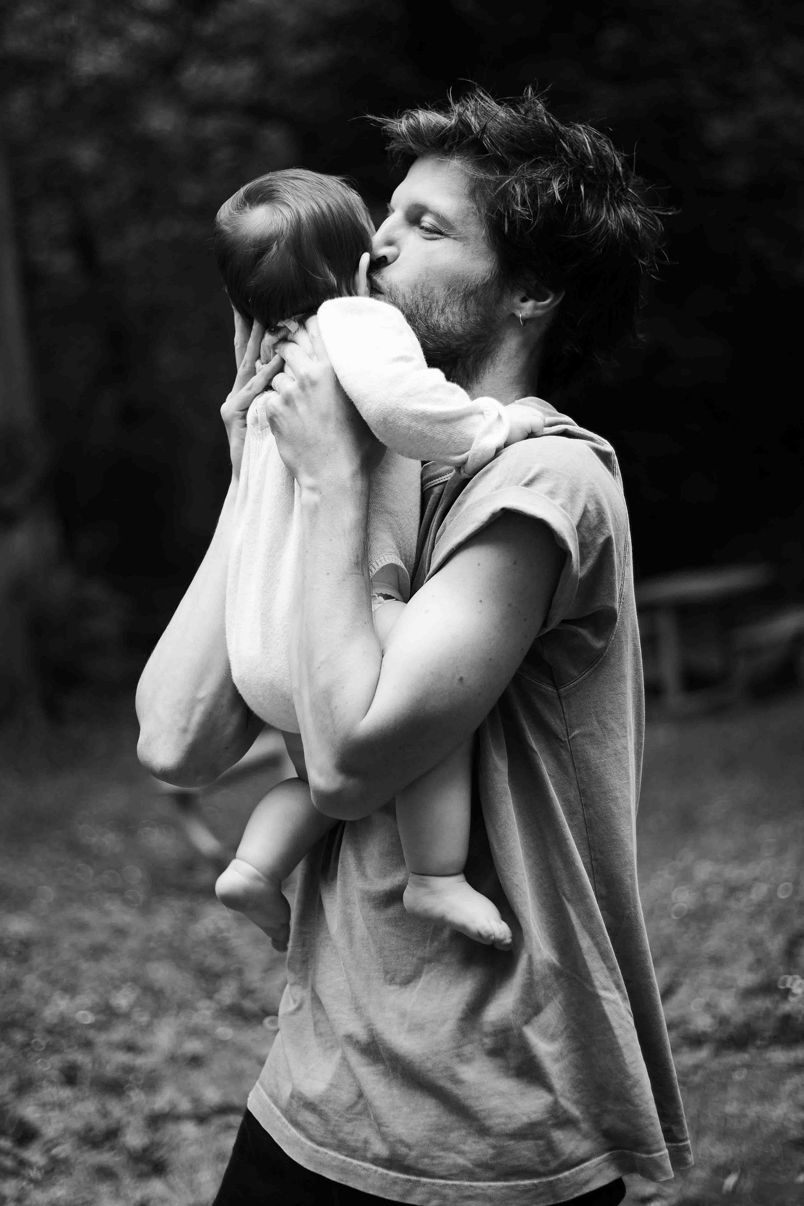 Un père tient son bébé dans les bras et lui fait un bisou lors d'une séance photo famille à Toulouse.