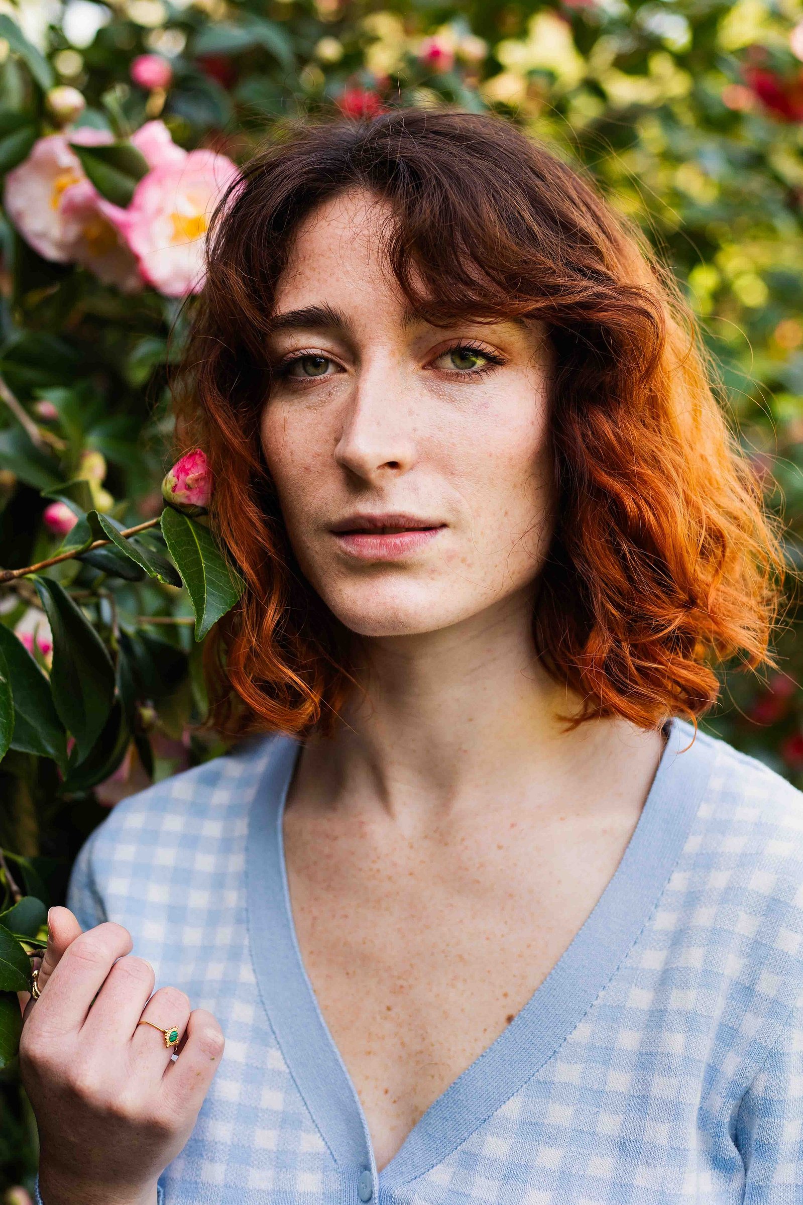 Une jeune femme rousse regarde droit devant elle à côté d'un arbuste en fleurs lors d'une séance photo à Toulouse.