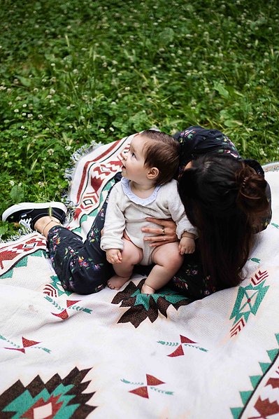 Une mère et son bébé joue sur une nappe dans l'herbe lors d'une séance photo famille à Toulouse.