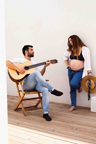 Une femme enceinte regarde son mari jouer de la guitare sur leur terrasse lors d'une séance photo grossesse à Toulouse