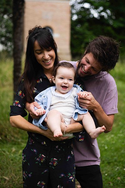 Des parents rigolent et tiennent leur bébé dans les bras lors d'une séance photo famille à Toulouse.