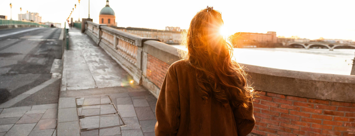 Une femme rousse est de dos et marche sur un pont à Toulouse 