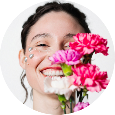 Une femme rit aux éclats en tenant un bouquet de fleurs roses devant son visage lors d'une séance photo portrait en studio à Toulouse.