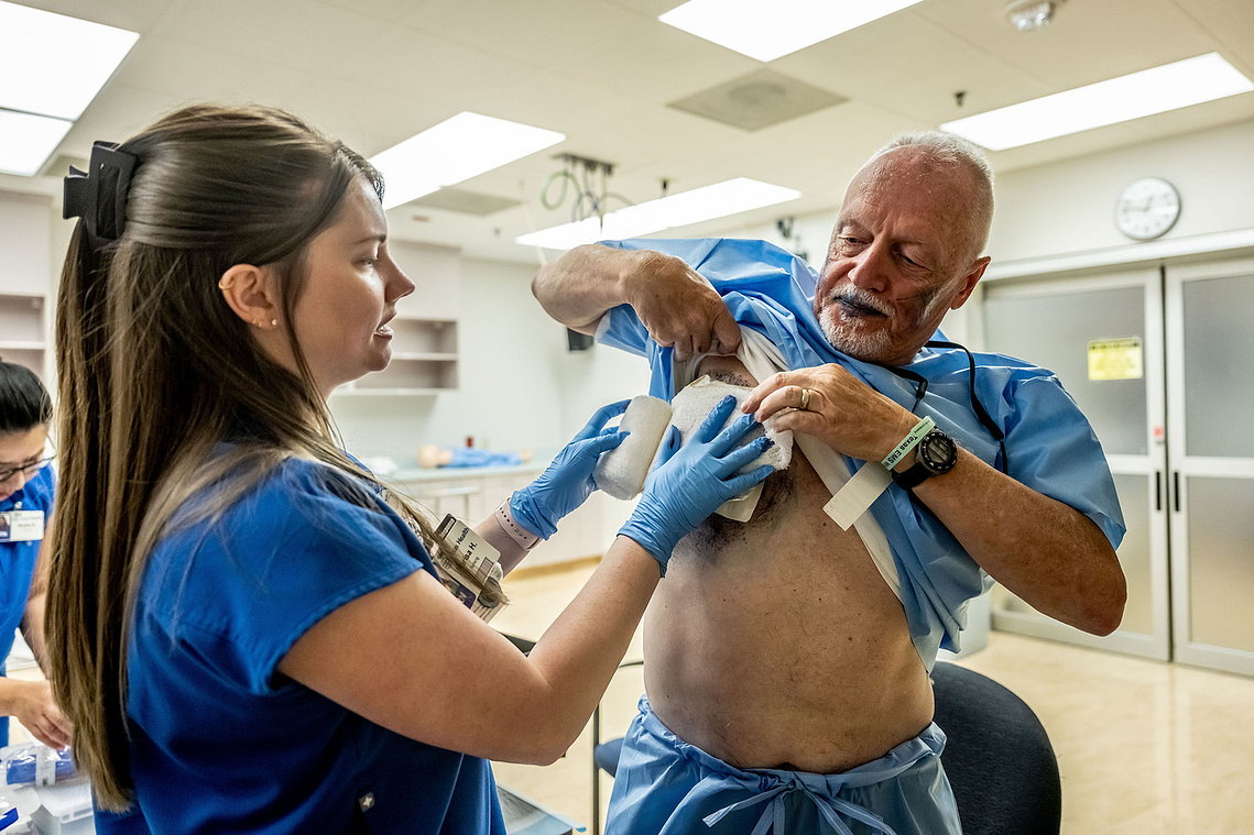A nurse applies simulated chest wounds during moulage preparation before a Mass Casualty Incident drill at Texas Health Presbyterian Hospital Dallas - realistic trauma makeup used to train emergency response teams in high-pressure medical scenarios.
