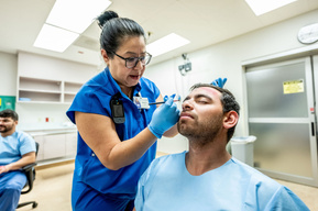 A nurse applies simulated facial injuries during moulage preparation for a Mass Casualty Incident drill at Texas Health Presbyterian Hospital Dallas - detailing the meticulous staging process used to create realistic emergency training scenarios.
