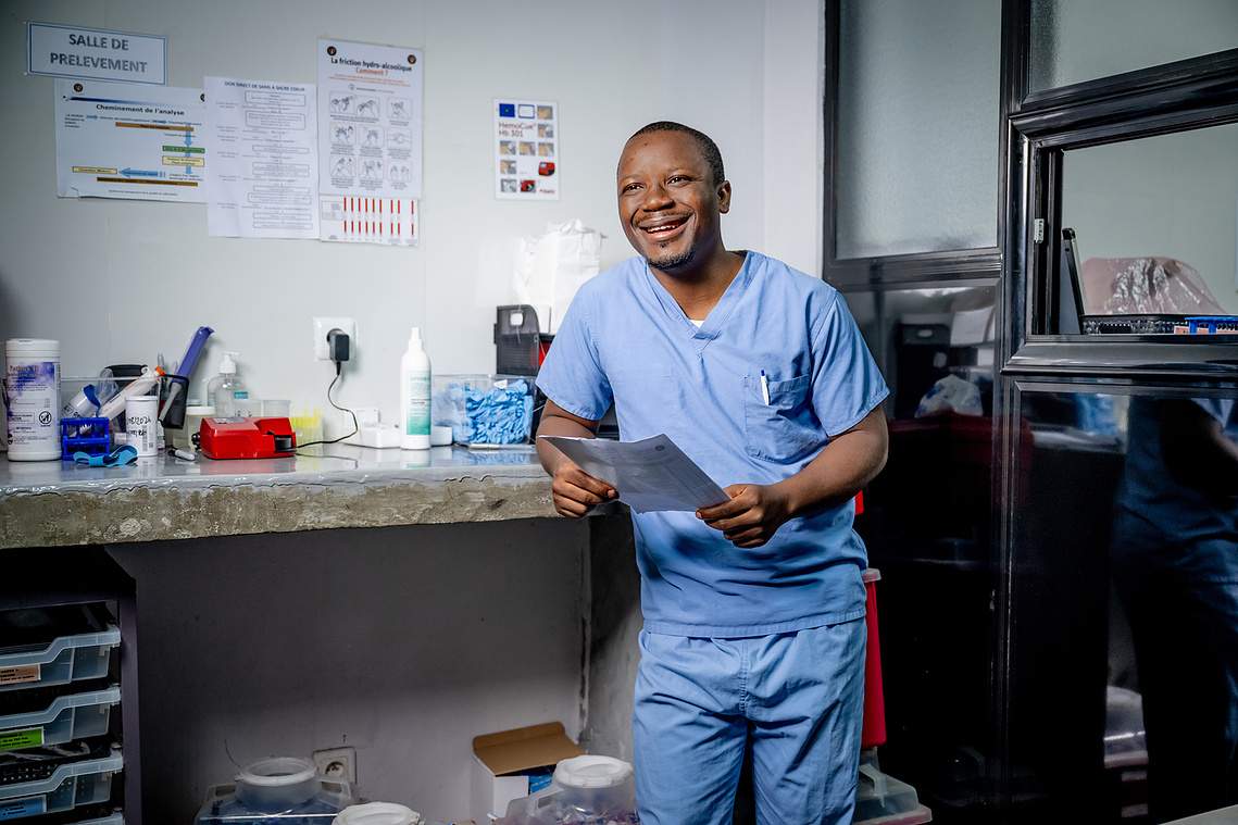Healthcare professional in blue scrubs smiling inside the Sacré Coeur medical clinic in Guinea, West Africa.