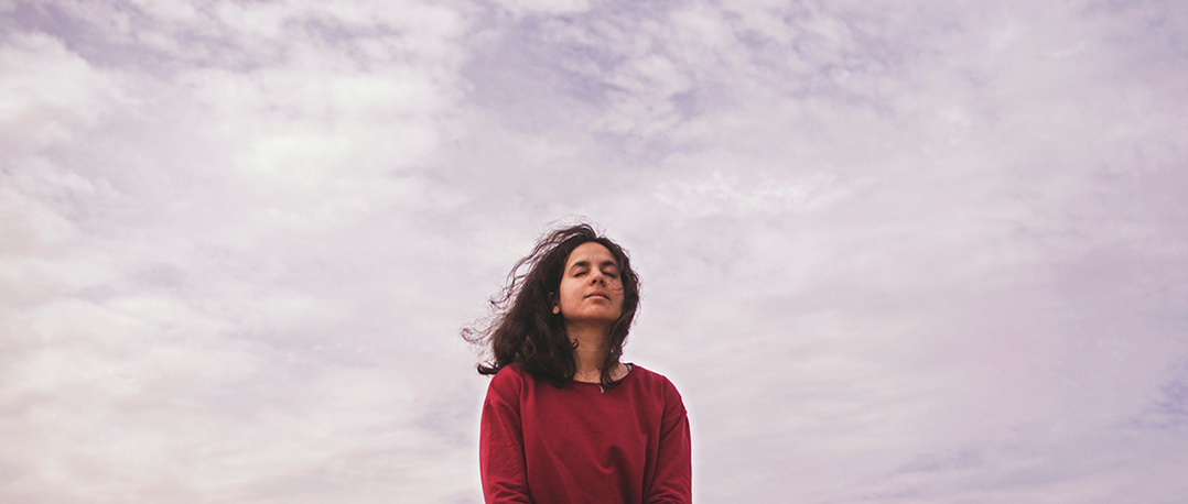 Portrait of a meditating young woman against cloudy sky