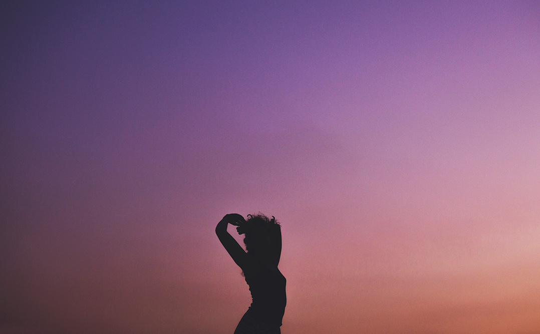 Silhouette of a dancing young woman against a violet sunset sky