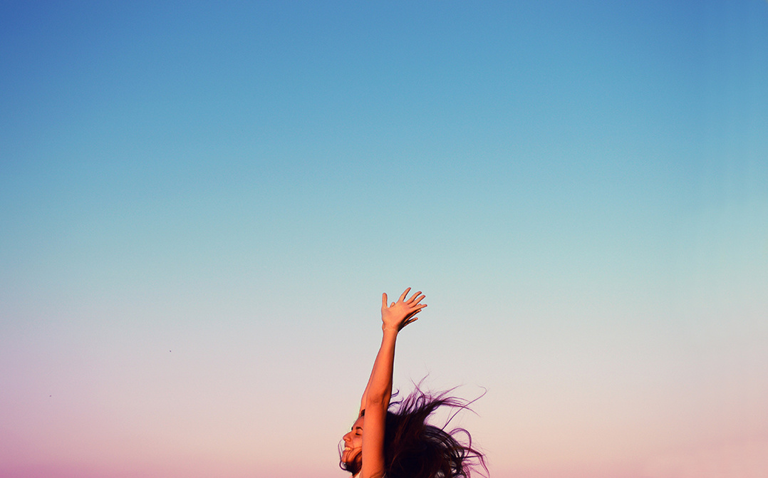 Girl jumping happily against soft hued sky