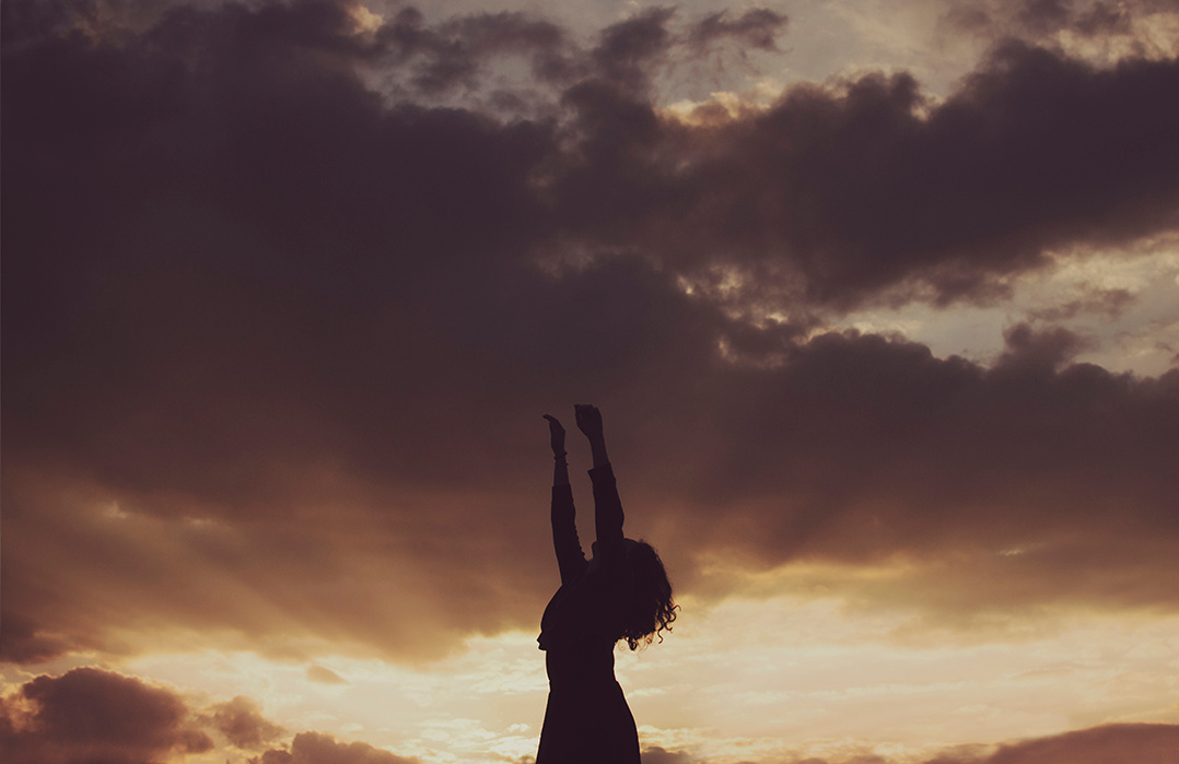 Silhouette of a young woman against a cloudy sunset sky