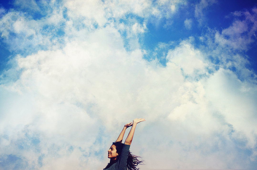 Jumping happy girl against cloudy blue sky