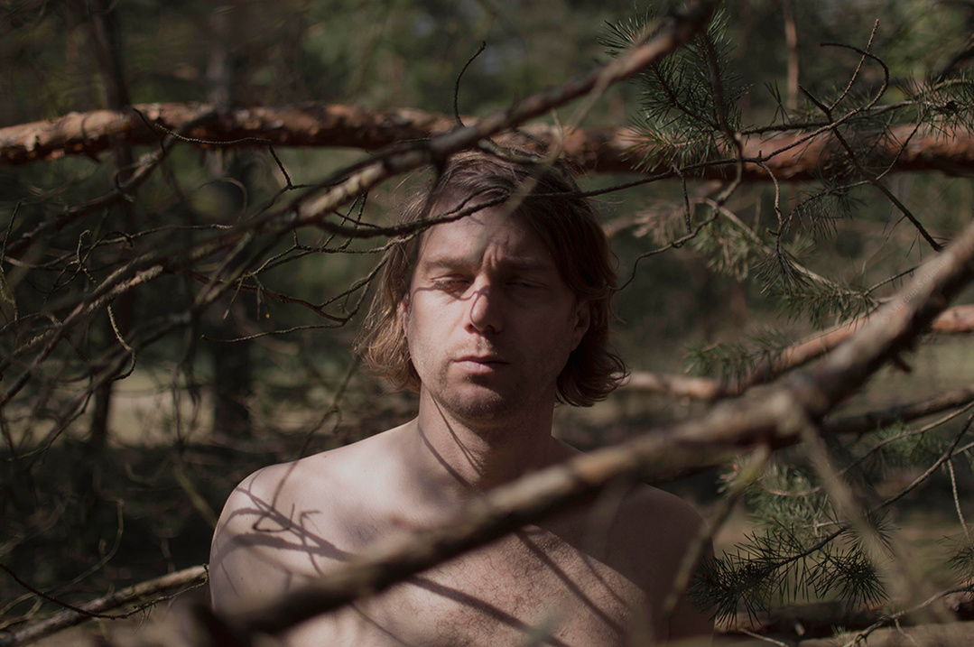 Delicate soft nude forest portrait of man between trees