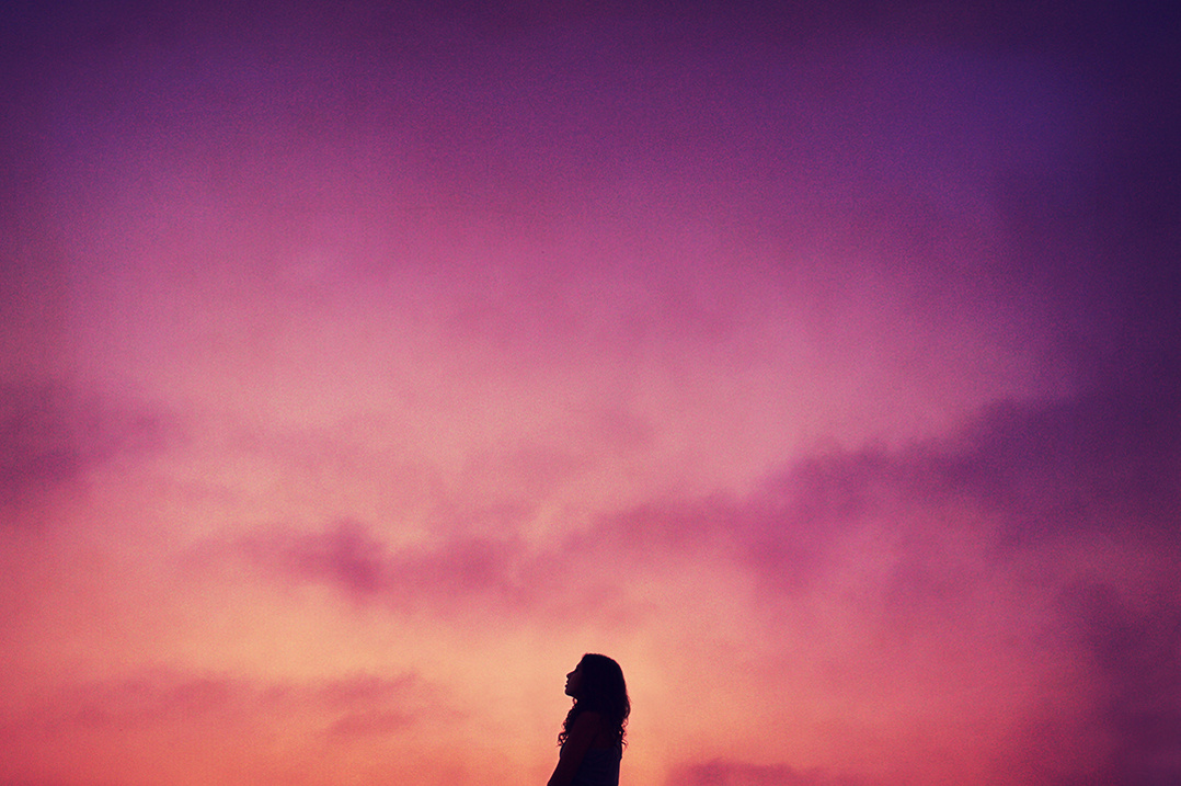 Silhouette of a young woman against a pink hued sunset sky