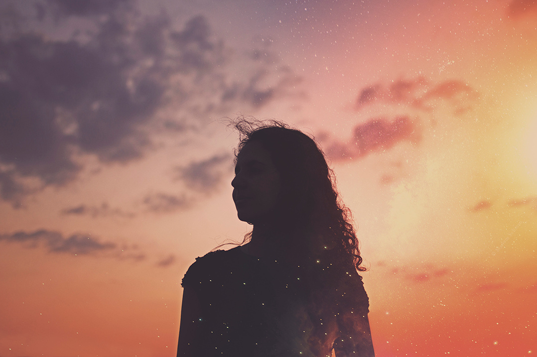 Silhouette of a young woman against a colorful sunset sky