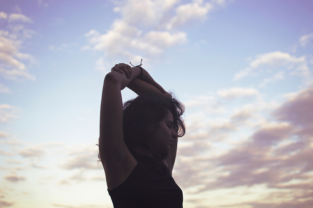 Silhouette of a woman embracing herself against a cloudy sunset sky