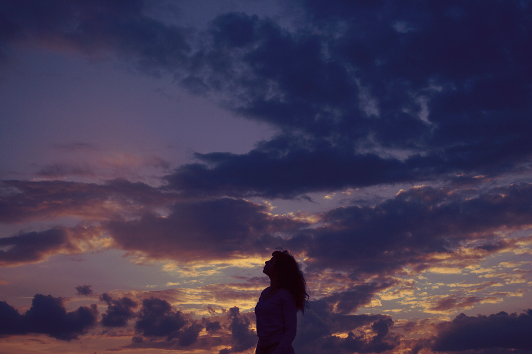 Silhouette of a young woman against a colorful cloudy sunset sky
