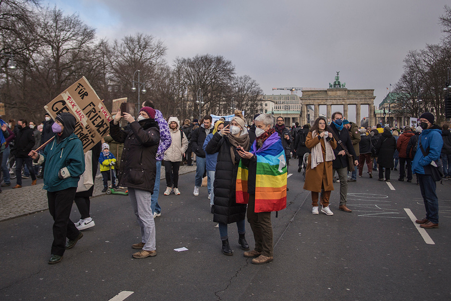Demonstrierende mit Regenbogenfahne schauen sich auf der Friedensdemo gegen den Ukraine-Krieg in Berlin am 27.02. um