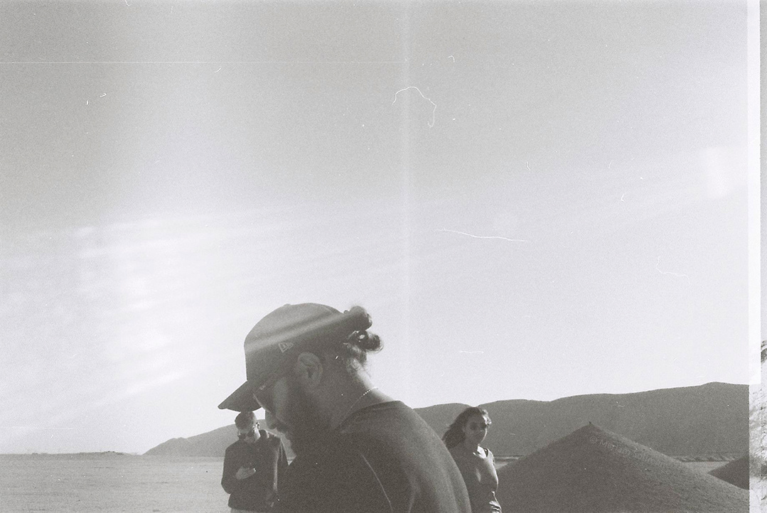 Analog black and white photograph of young man with black apparel in the desert