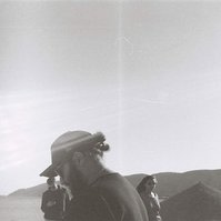Analog black and white photograph of young man with black apparel in the desert