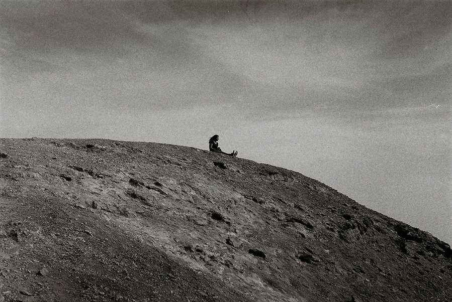 Analog black and white photograph of woman sitting on top of desert hills in Wadi Degla, Egypt