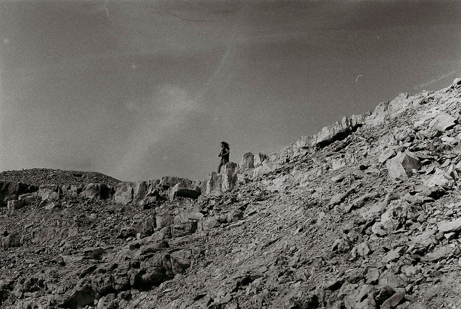 Analog black and white photograph of woman standing on top of desert hills in Wadi Degla, Egypt