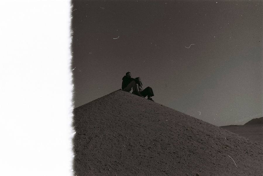 Analog black and white photograph of couple sitting on top of desert hills in Egypt