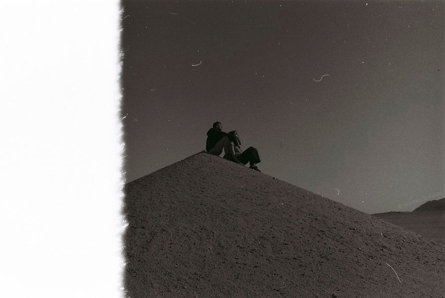 Analog black and white photograph of couple sitting on top of desert hills in Egypt