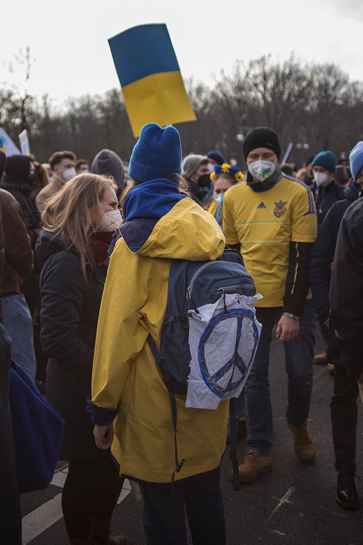 Demonstrierende trägt blau-gelbe Kleidung und hält blau-gelbes Schild auf der Friedensdemo gegen den Ukraine-Krieg in Berlin am 27.02. 