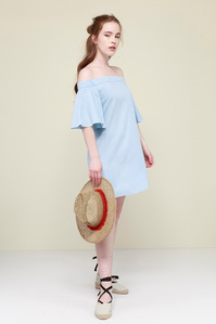 model in blue dress holding straw hat on plain background