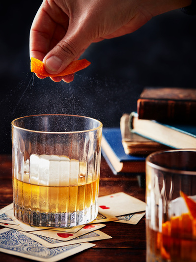 An old fashioned with a hand spritzing oramge peel, perfect for editorial, advertising and restaurant food photography, shot by food photographer, Sid Ali