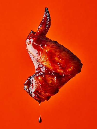 A floating chicken wing on bright orange background, perfect for editorial, advertising and restaurant food photography, shot by food photographer, Sid Ali