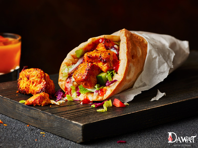 A chicken tikka kebab roll shot on a dark chopping board with scattering of food, perfect for editorial and restaurant food photography, shot by food photographer, Sid Ali