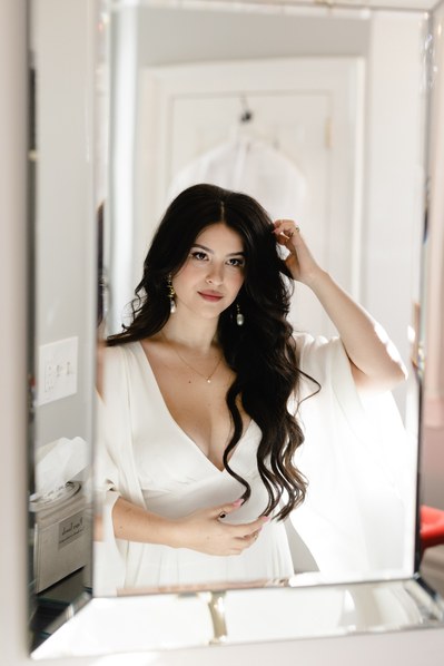 Beautiful brunette bride with Hollywood waves admiring herself in the mirror.