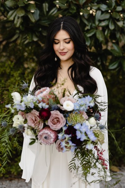 Gorgeous brunette bride holding flowers in a forest green environment.