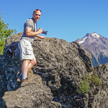 Landscape and wildlife photographer, Tom Fenske, poses in a remote mountain setting, camera in hand.