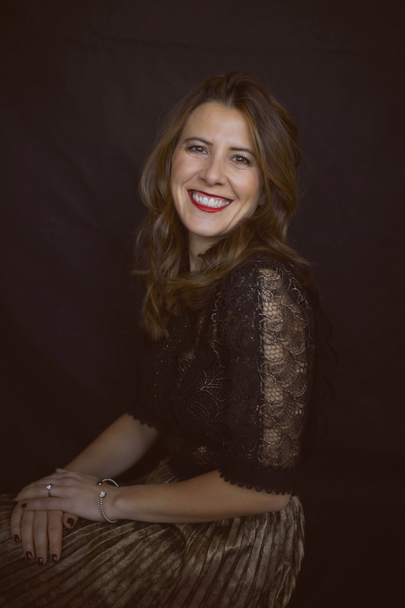 Professional studio portrait of a woman wearing a black and gold dress against a black studio backdrop