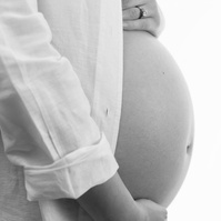Professional Maternity photograph of a womans pregnant belly, wearing white shirt against a white backdrop.