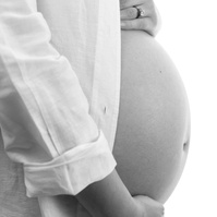Professional Maternity photograph of a womans pregnant belly, wearing white shirt against a white backdrop.