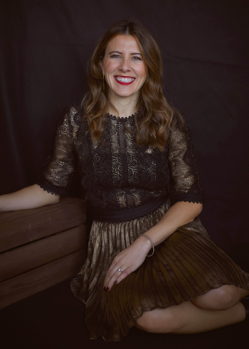 Professional studio portrait of a woman wearing a black and gold dress against a black studio backdrop