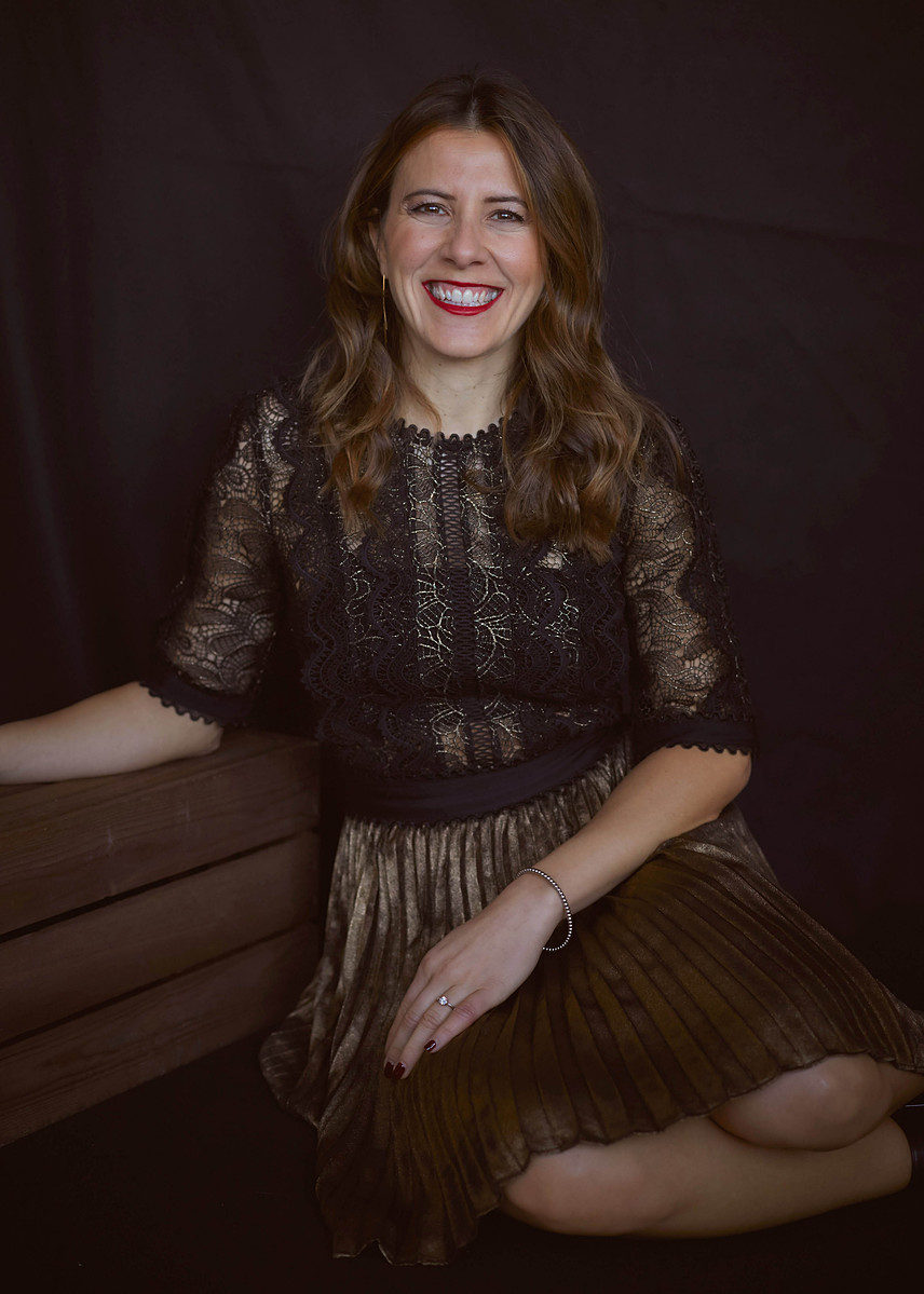 Professional studio portrait of a woman wearing a black and gold dress against a black studio backdrop