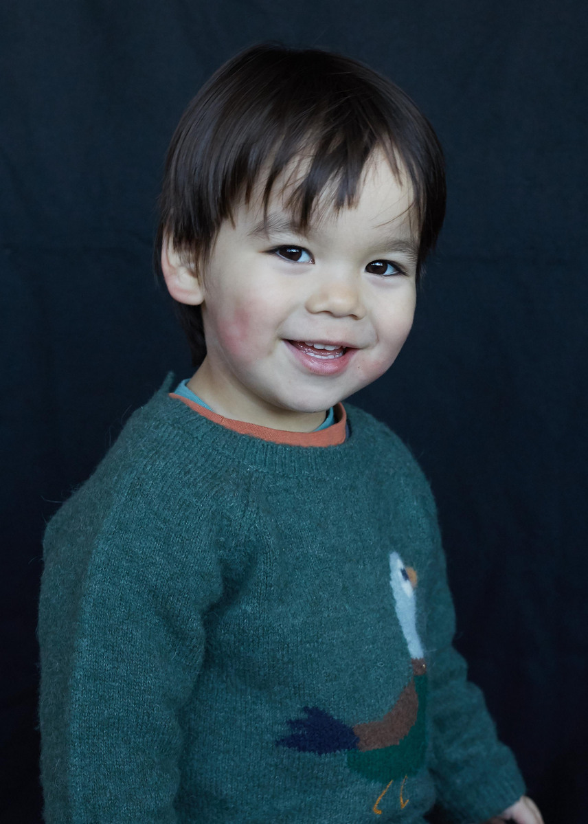 Portrait of a toddler boy wearing green jumper on a black studio background