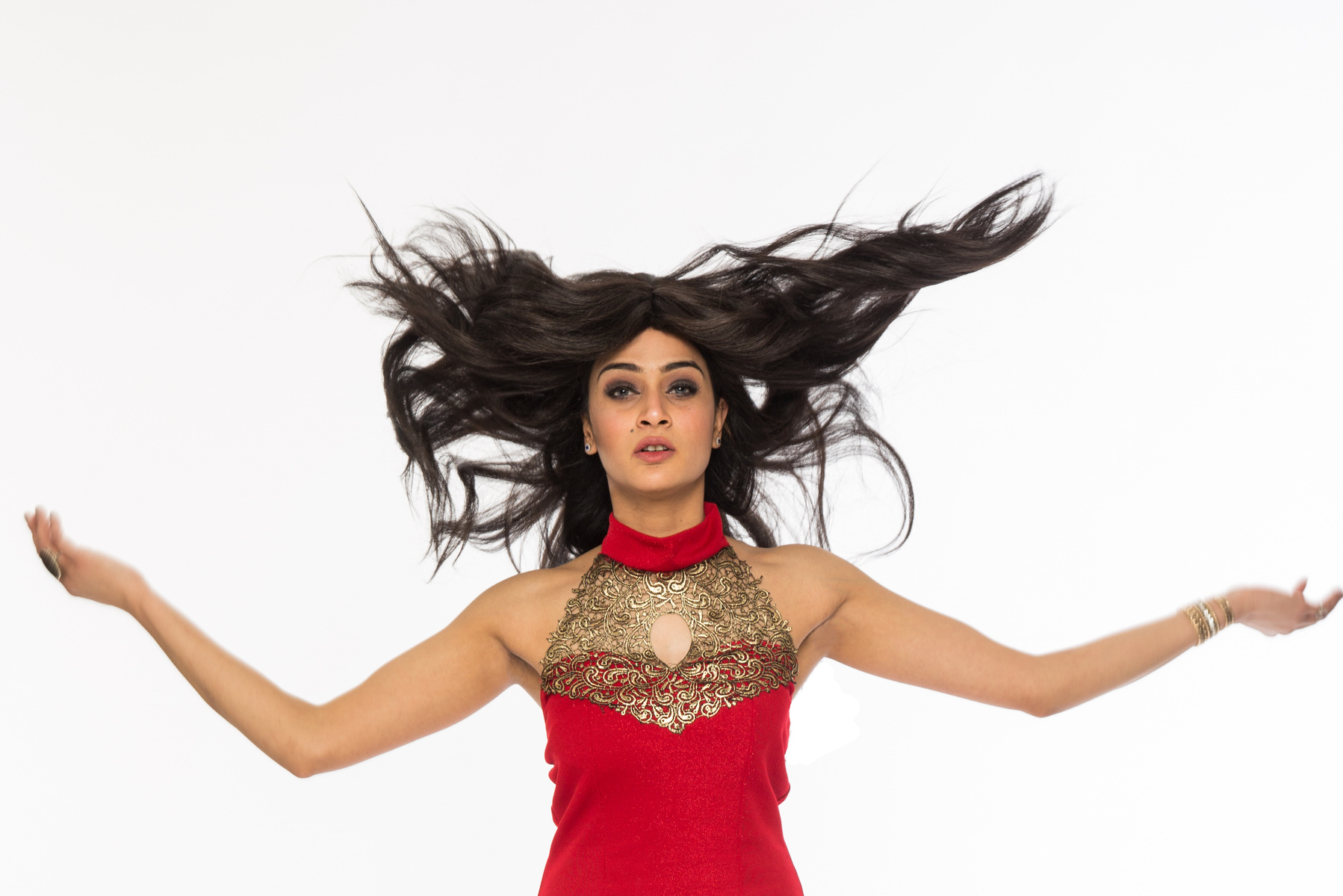 Professional photography studio portrait of a woman jumping wearing a red dress and hair flying in the air