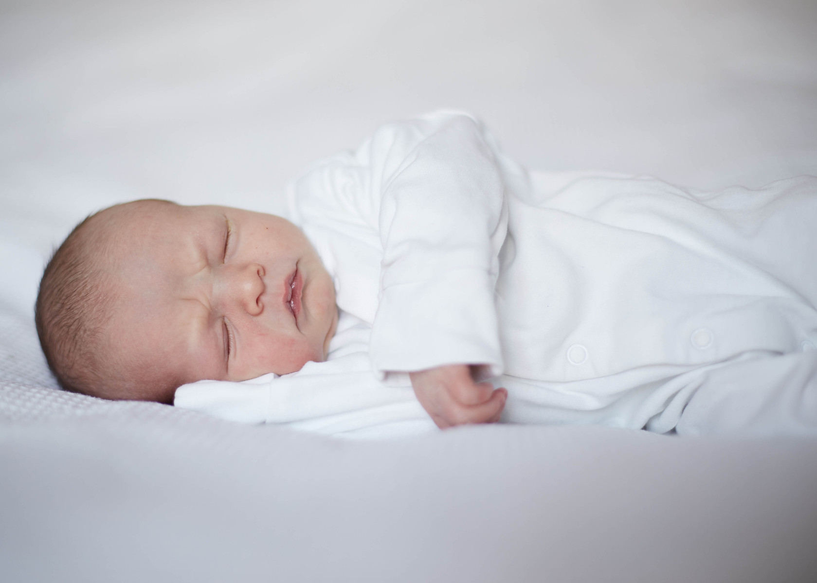 Newborn photograph of a baby wearing white on white background