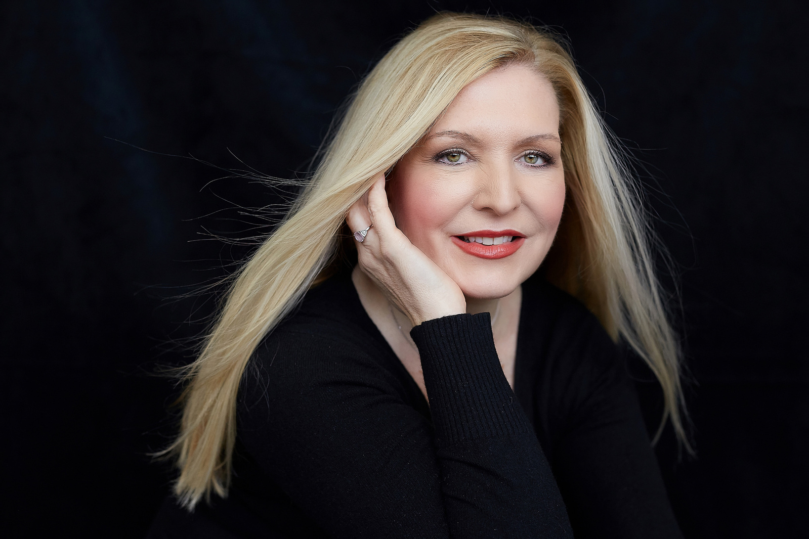 Award winning portrait of a blonde woman wearing a black top against a black  photography studio backdrop